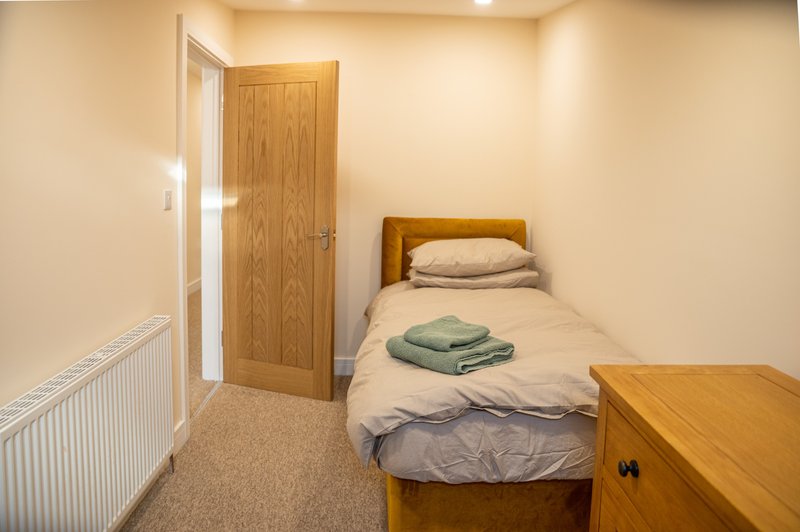 Compact bedroom with single bed, wooden door, radiator and small wooden cabinet