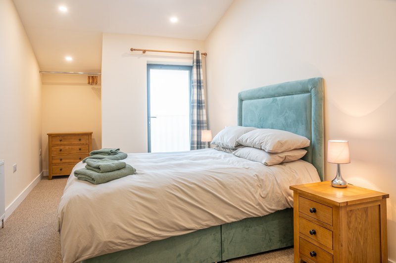 Bedroom with double bed, teal headboard, wooden nightstand and chest of drawers