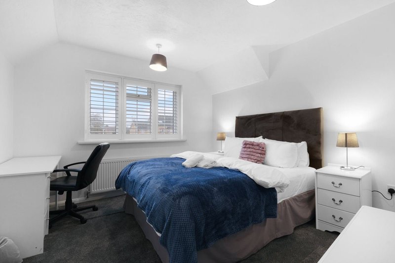 Bright bedroom with double bed, blue throw, desk chair, white shuttered window and bedside tables
