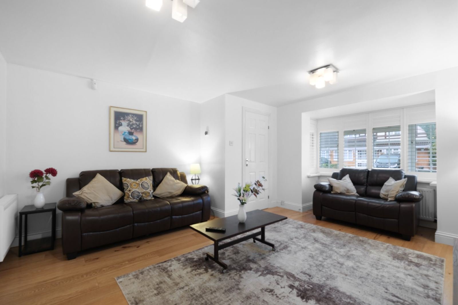 Bright living room with two dark leather sofas, wooden flooring, coffee table and large windows