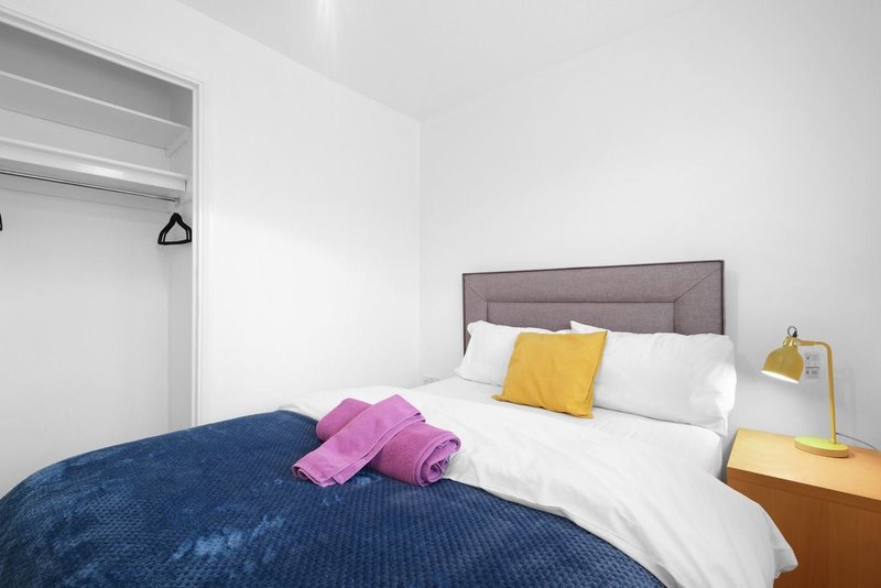 Modern bedroom with double bed, colorful pillows, wooden nightstand and brass lamp