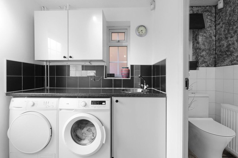 Compact bathroom with washing machine, dryer, white cabinets and black tile backsplash