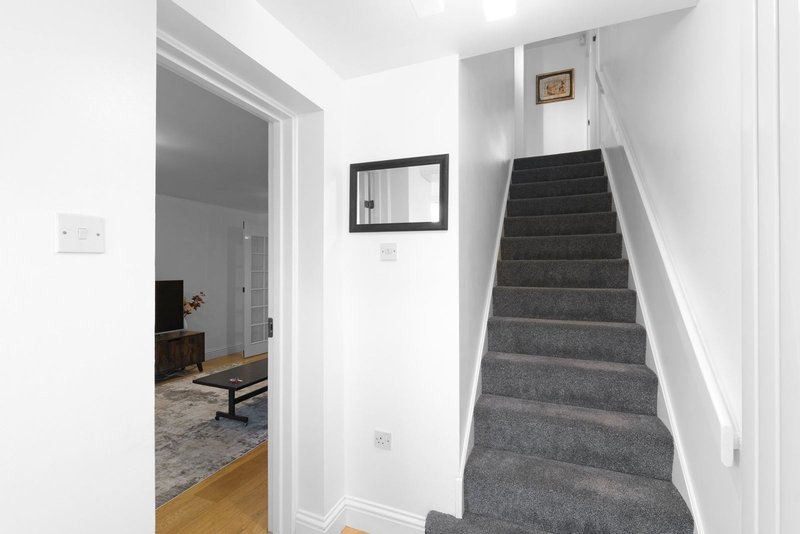 Hallway with staircase, white walls, grey carpet stairs and doorway to living room