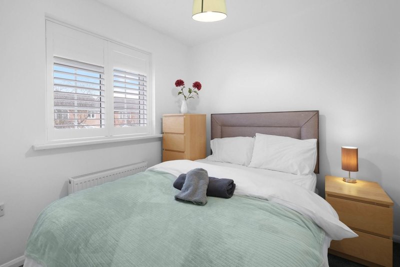 Bright bedroom with double bed, green bedspread, wooden nightstands and shuttered window