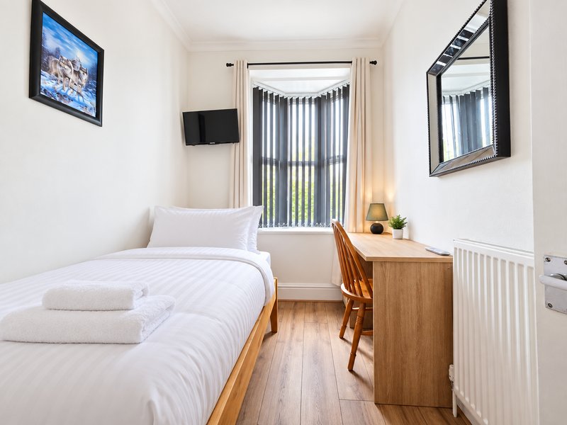 Bright bedroom with single bed, wooden desk, chair, wall-mounted TV and large mirror