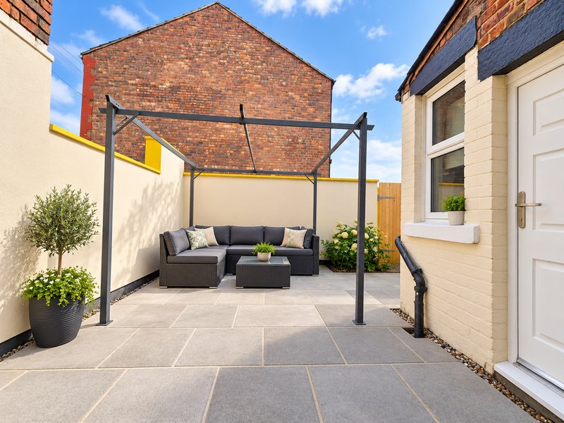 Paved courtyard with black pergola, blue seating, potted plants and brick building backdrop