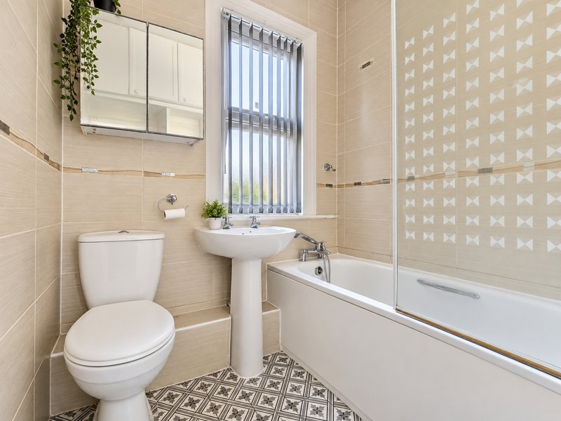 Clean modern bathroom with toilet, pedestal sink, bathtub and vertical blinds window