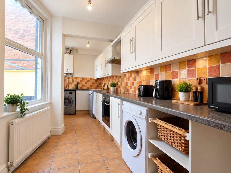 Modern kitchen with white cabinetry, orange tile backsplash, two washing machines, and natural light from window