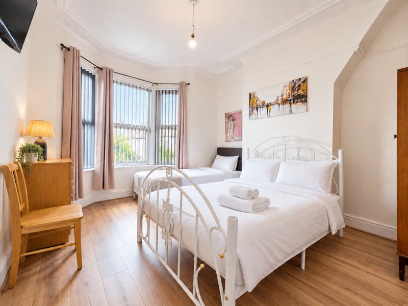 Bright bedroom with two white metal-frame beds, wooden furniture, and glass doors to garden