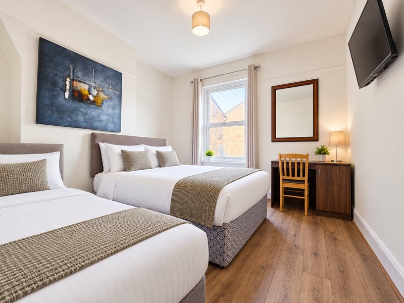 Twin bedroom with two beds, wooden floor, wall art, and window with natural light