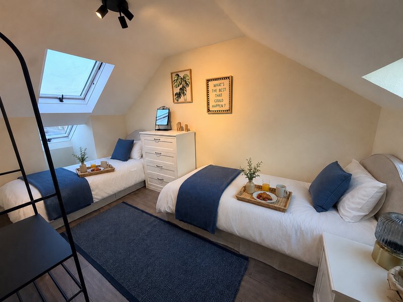 Bright attic bedroom with two single beds, white bedding, blue cushions and runner rug
