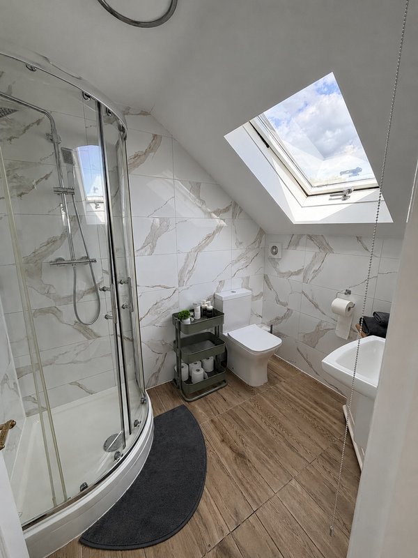 Modern bathroom with curved shower enclosure, toilet, sink and skylight window