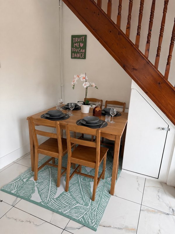 Compact wooden dining table with two chairs, place settings, and flowers under staircase