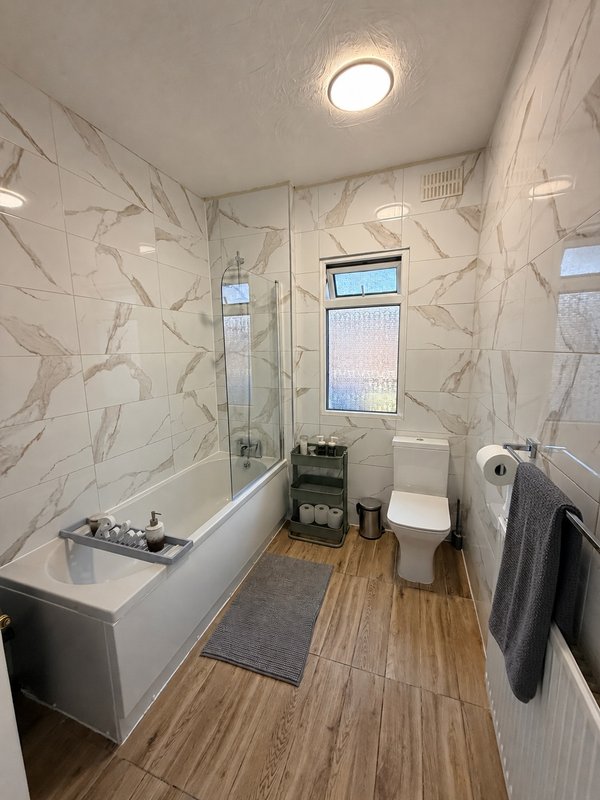 Modern bathroom with white marble-effect tiles, bathtub, toilet, and wooden-effect flooring