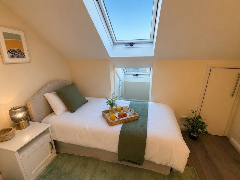 Bright attic bedroom with skylight, double bed, bedside lamp and small potted plant