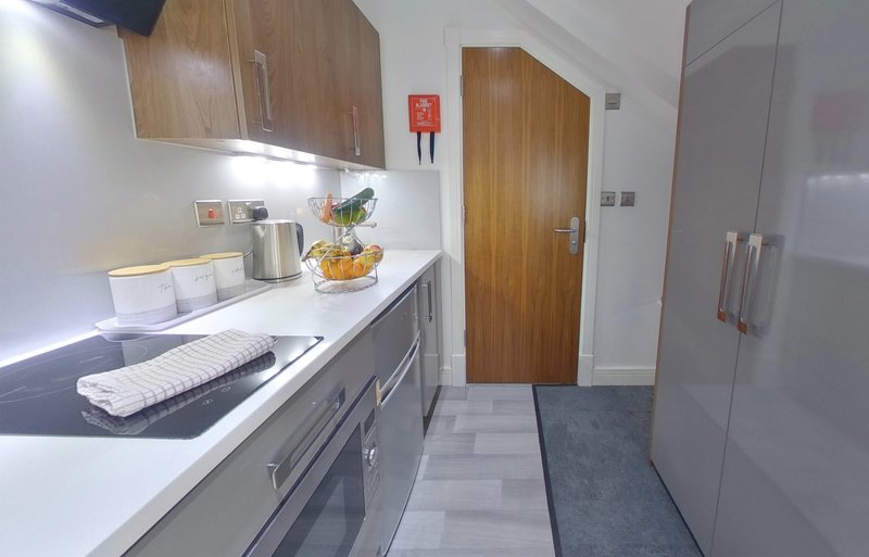 Modern galley kitchen with white countertops, wooden cabinets, kettle, and wooden door