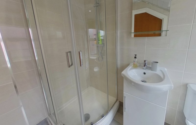 Modern bathroom with corner shower enclosure, white sink, and wooden shelf