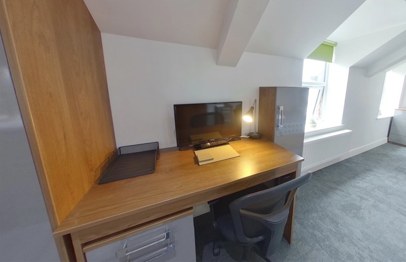 Home office with wooden desk, monitor, chair and natural light from windows