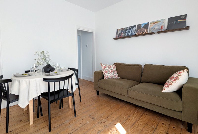 Open-plan living room with olive sofa, dining table with black chairs, wooden floor