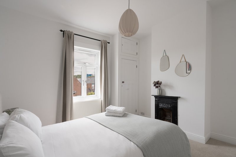 Bright bedroom with double bed, white bedding, pendant lamp, and decorative mirrors on wall