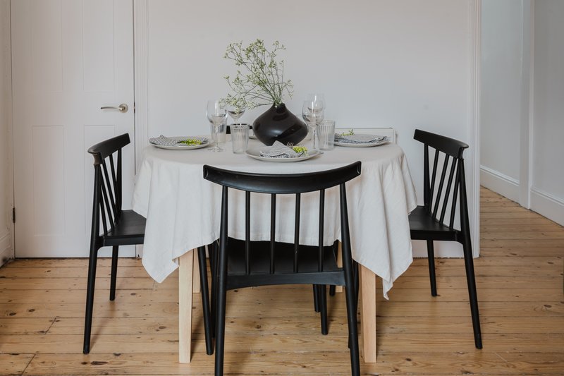 Dining table set with white tablecloth, black chairs, place settings and floral centerpiece