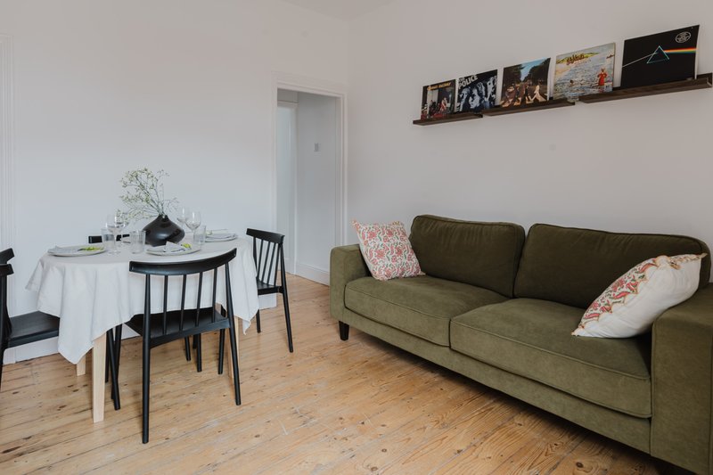 Open-plan living room with green sofa, dining table, wooden floor and wall shelving