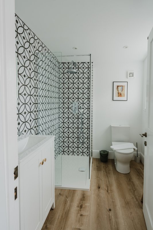 Modern bathroom with geometric tile shower, white vanity, toilet, and wood-look flooring