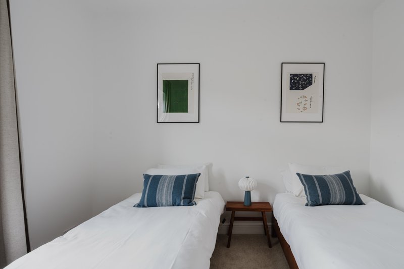 Twin bedroom with white bedding, striped pillows, wooden nightstand and framed wall art