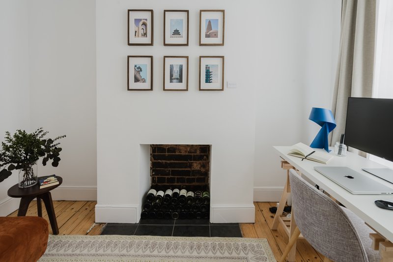 Bright living room with fireplace, framed wall art, desk with monitor, and potted plant