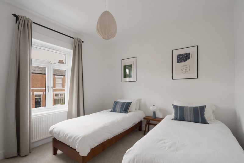 Twin bedroom with two single beds, striped pillows, pendant lamp, and window view