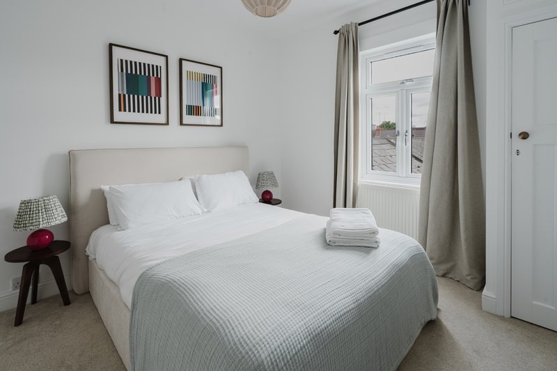 Bright bedroom with queen bed, upholstered headboard, framed wall art and garden view