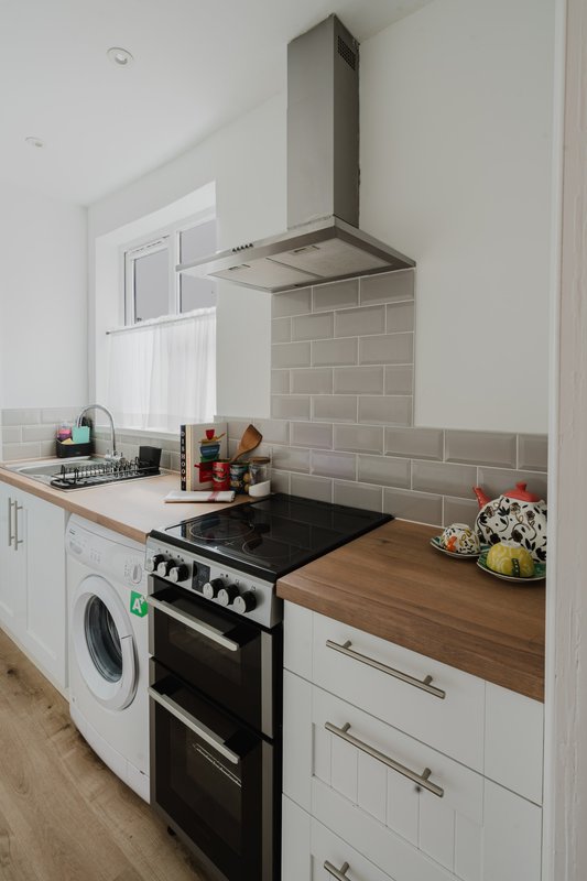Modern kitchen with white cabinets, black double oven, stainless steel cooker hood and subway tile backsplash