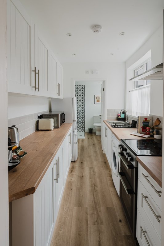 Modern galley kitchen with white cabinetry, wooden countertops, stainless steel appliances and wood flooring