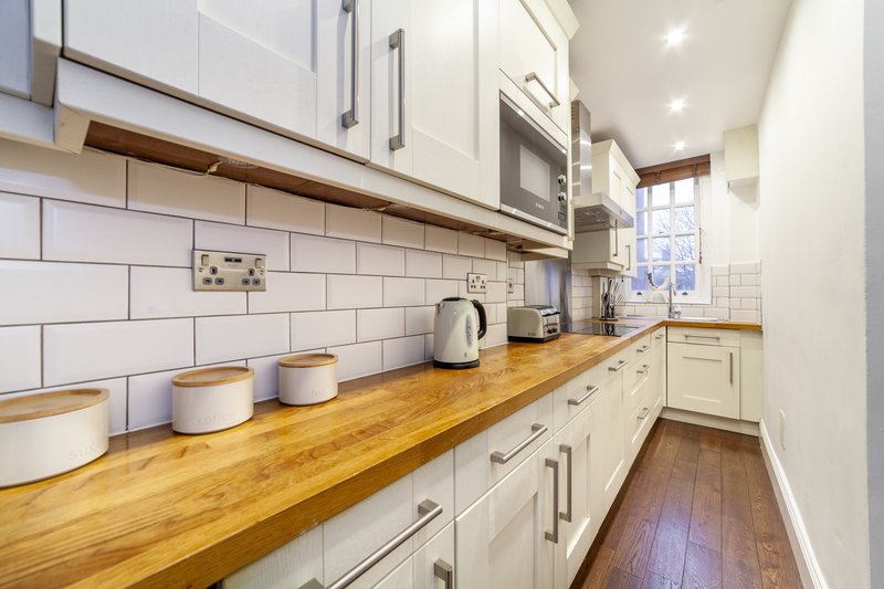 Modern galley kitchen with white cabinetry, wooden countertop, subway tile backsplash and appliances