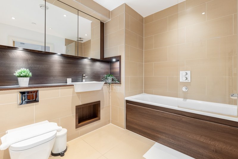Modern bathroom with vanity sink, toilet, bathtub, mirrored cabinet and beige tile walls