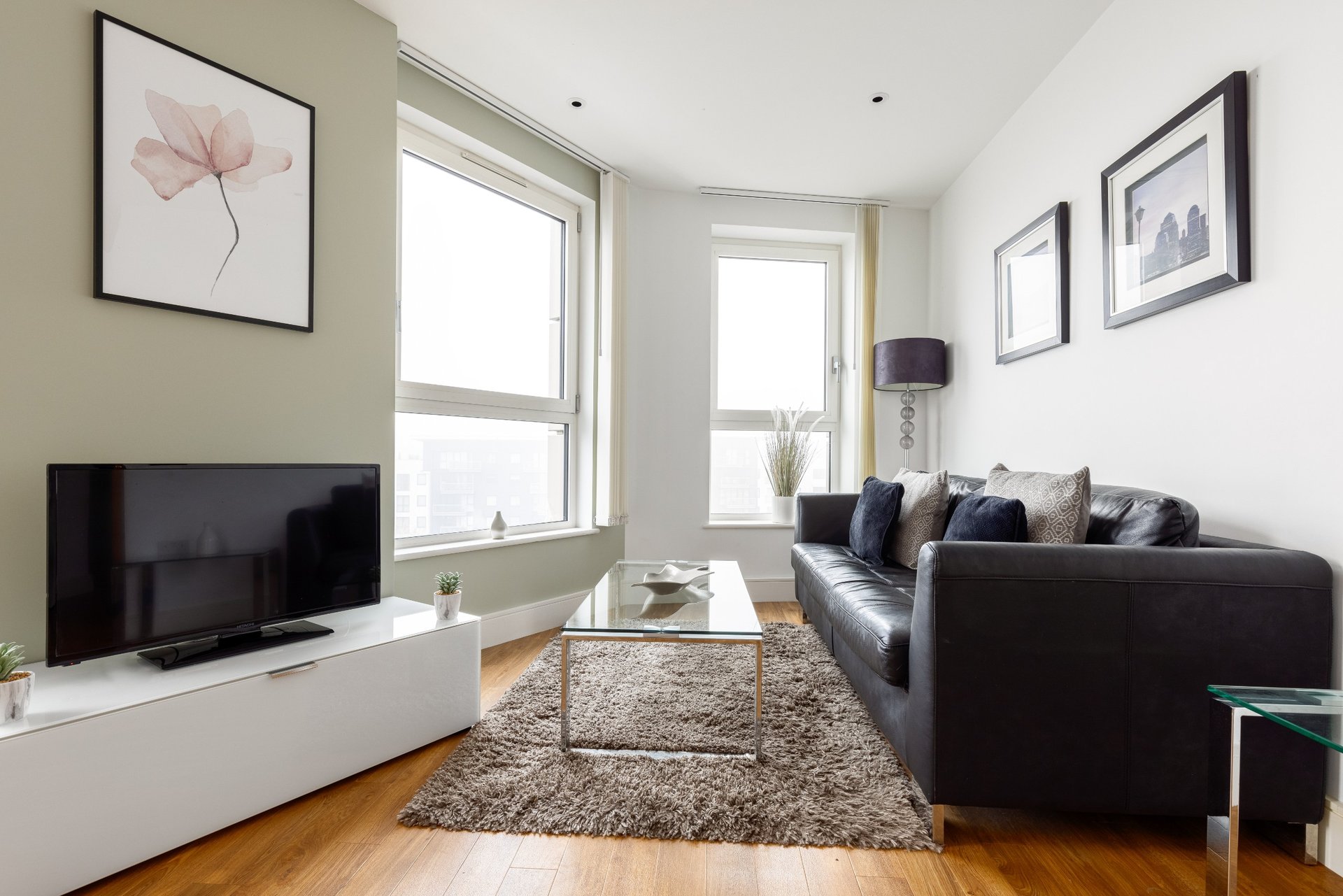Modern living room with black sofa, TV unit, wooden floor and framed wall art
