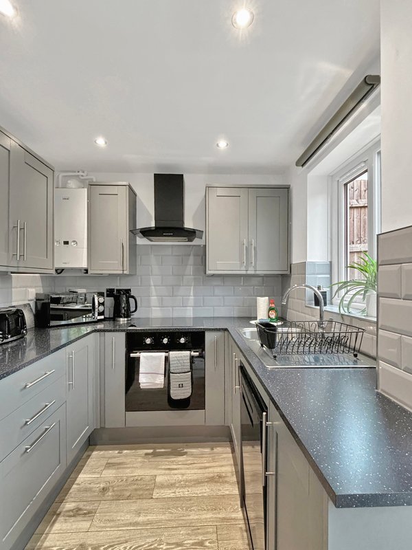 Modern galley kitchen with light grey cabinets, black oven, stainless steel sink and worktops