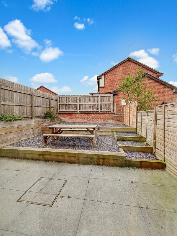 Brick house rear garden with patio, wooden bench, and fenced boundaries