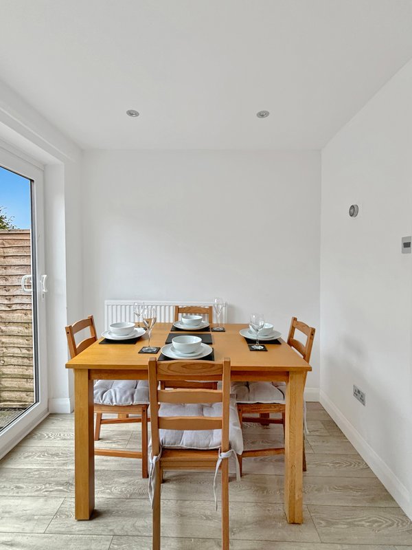 Dining room with wooden table, four chairs, place settings, and glass door to garden