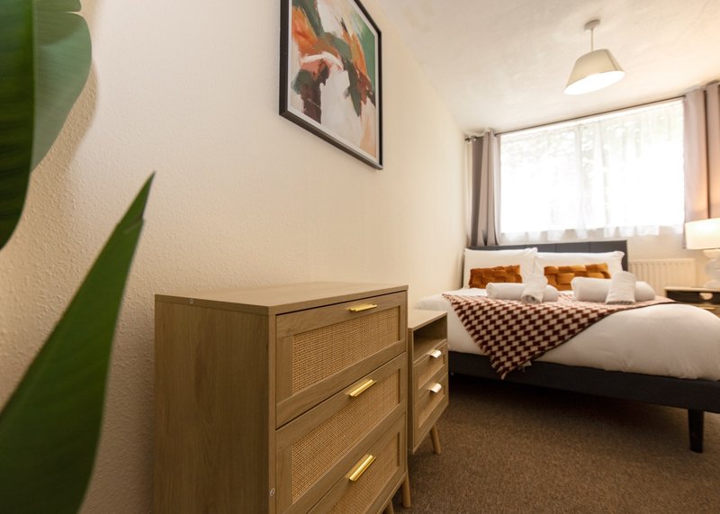 Bedroom with wooden dresser, double bed, green plant, and window with curtains