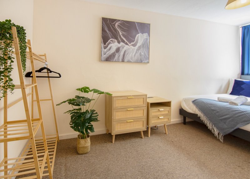 Spacious bedroom with wooden bed frame, dresser, potted plant, and blue curtains
