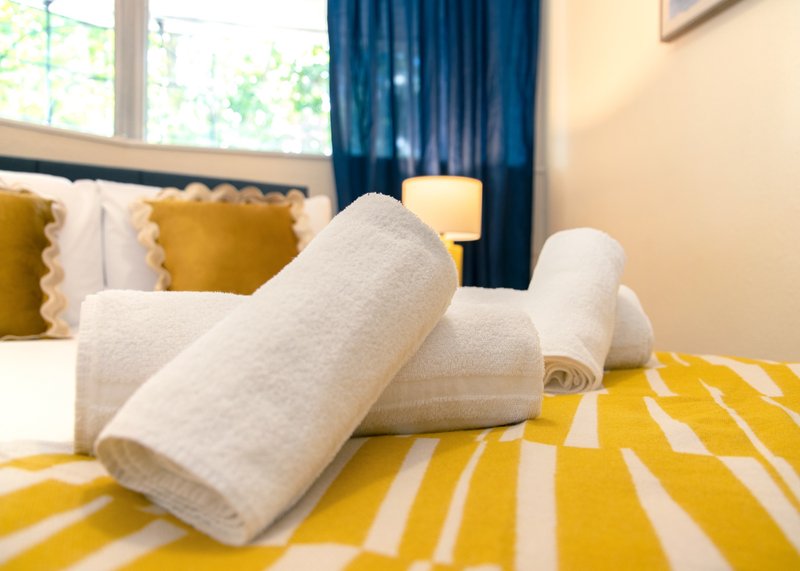 Bedroom with yellow striped bed, white towels, gold cushions and blue curtains