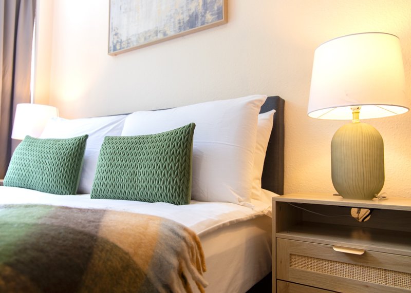 Bedroom with double bed, green cushions, bedside lamp and framed wall art