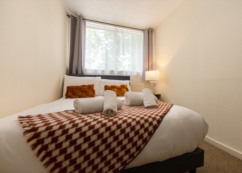 Bedroom with double bed, patterned throw, cushions, window with curtains and bedside lamp