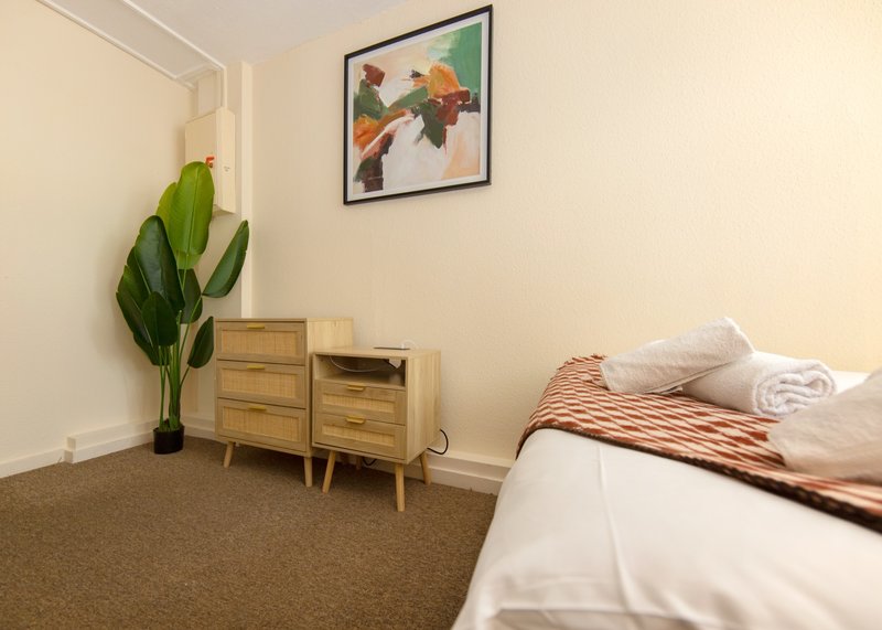 Bedroom with double bed, wooden nightstands, potted plant, and framed artwork on wall