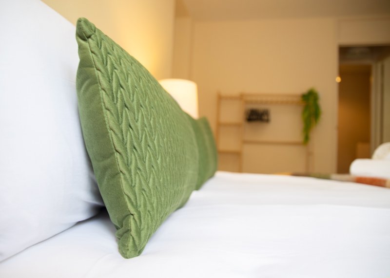 Bedroom with white bedding, green decorative pillow, and warm lighting