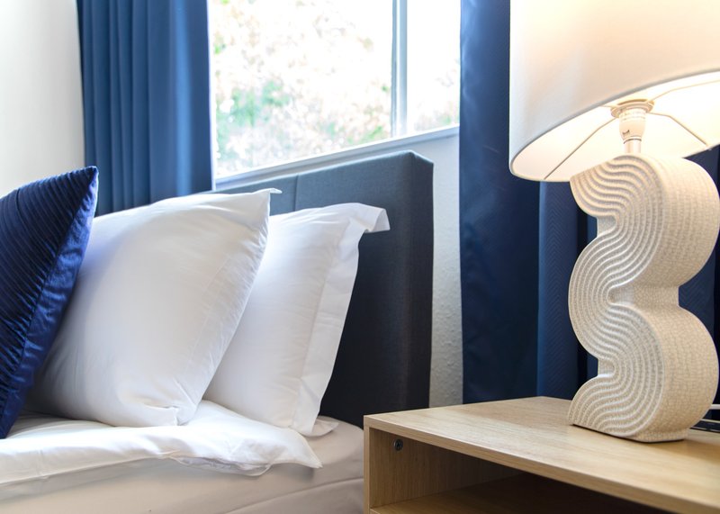 Modern bedroom with white pillows, dark headboard, blue curtains and wooden nightstand