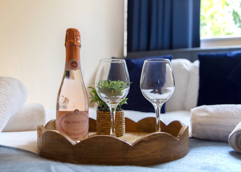 Prosecco bottle with wine glasses and fresh mint in wooden tray on bed