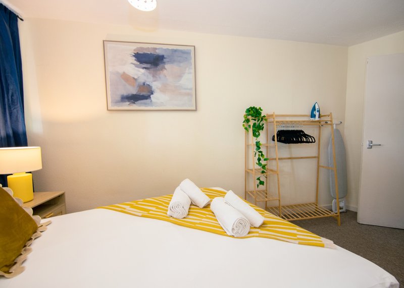 Modern bedroom with double bed, yellow bedding, white pillows, framed wall art and wooden clothing rack