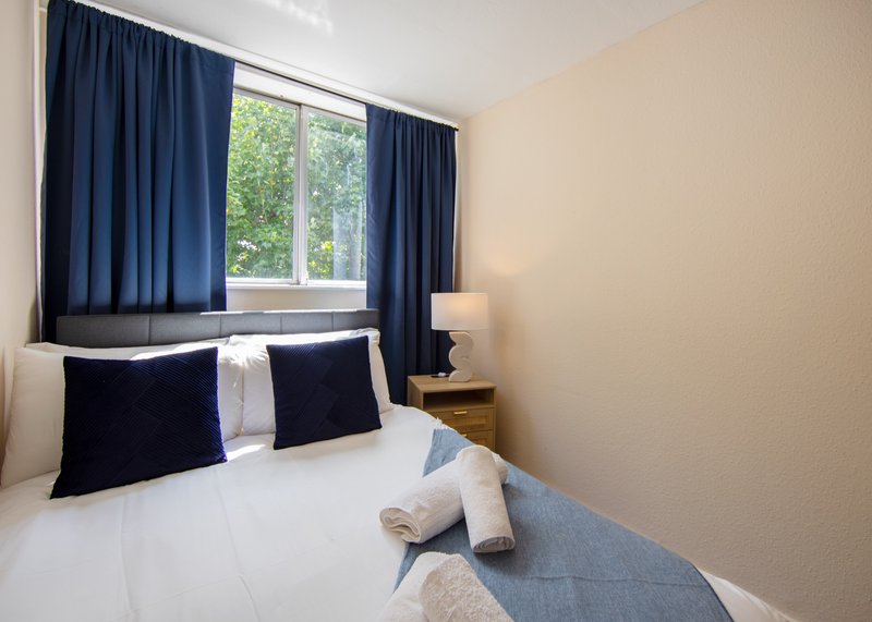 Bright bedroom with double bed, navy pillows, white bedding, navy curtains and window view